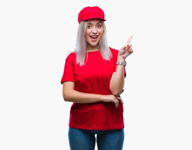 Kameraya bakarak yan el ve parmak ile işaret yüzünde kocaman bir gülümseme ile izole arka plan üzerinde kırmızı şapkalı sarışın genç kadın.