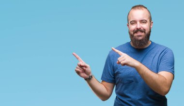 Genç beyaz hipster adam gülümseyerek ve iki elleri ve parmakları ile tarafına işaret kamera bakarak izole arka plan.