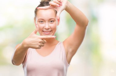 Genç beyaz güzel kadın elle yapma çerçeve ve parmakları ile mutlu yüz gülümseyen izole arka plan yüzünden. Yaratıcılık ve Fotoğrafçılık kavramı.