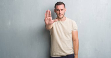 Genç beyaz adam açık eliyle dur işareti ile ciddi ve kendine güvenen ifade, savunma jest yapıyor gri grunge duvarın üzerinden