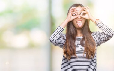 Genç Asyalı kadın dilini, parmaklarının arasından baktığını yapışmasını dürbün gibi ok jest yapıyor izole arka plan üzerinde gözlük takıyorum. Deli ifade.