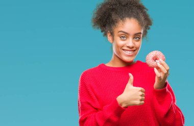 Genç afro Amerikalı kadın ok işareti, başparmak ile parmak, mükemmel işareti yapıyor kocaman bir gülümseme ile izole arka plan üzerinde mutlu donut yemek