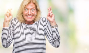 Orta yaş sarışın kadın geçiş parmakları umut ve gözler gülümseyen izole arka plan yüzünden kapalı. Şans ve batıl kavramı.