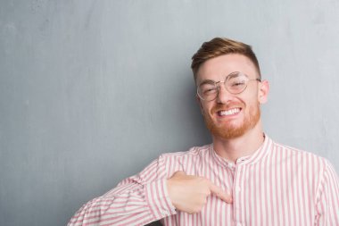 Genç Kızıl saçlı adam kendisi için sürpriz yüz işaret parmağı ile gri grunge duvarın üzerinden