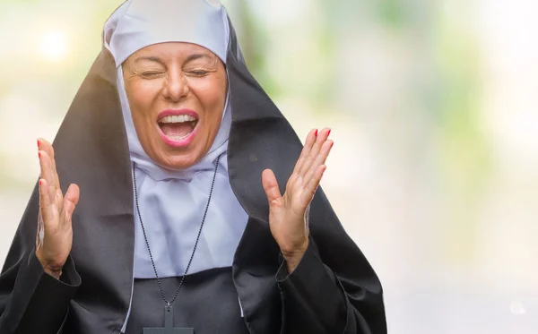 Middle age senior christian catholic nun woman over isolated background celebrating mad and crazy for success with arms raised and closed eyes screaming excited. Winner concept