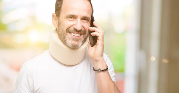 受伤的资深男子使用一个颈部支撑愉快的交谈使用智能手机 — 图库照片