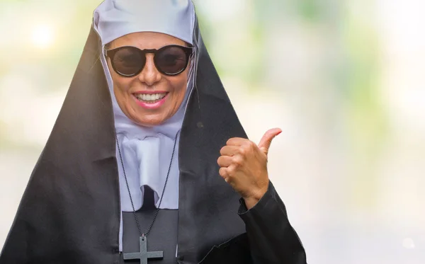 探していると親指側に上向きの幸せそうな顔を浮かべて孤立の背景の上にサングラスをかけている中年シニアのカトリック修道女女 — ストック写真