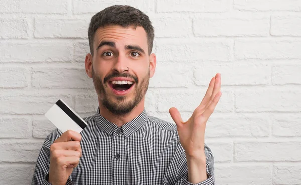 Joven Adulto Sobre Pared Ladrillo Sosteniendo Tarjeta Crédito Muy Feliz —  Fotos de Stock