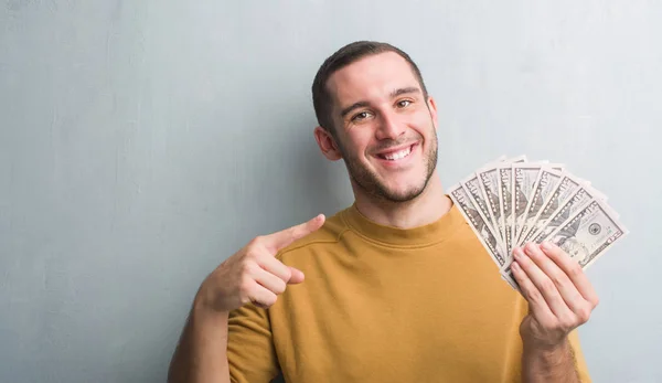 Young Caucasian Man Grey Grunge Wall Holding Dollars Very Happy — Stock Photo, Image