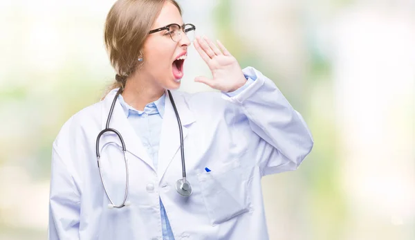Beautiful young blonde doctor woman wearing medical uniform over isolated background shouting and screaming loud to side with hand on mouth. Communication concept.