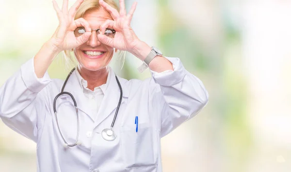 中年金发医生妇女在孤立的背景做 手势像望远镜伸出舌头 眼睛看通过手指 疯狂的表情 — 图库照片