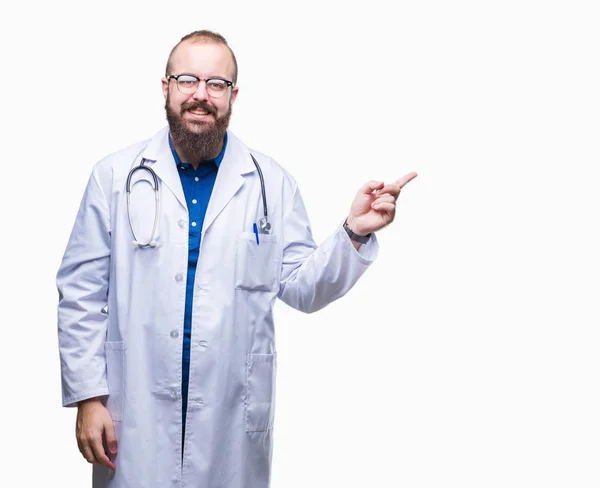 若い白人の医者の男の顔に大きな笑みを浮かべて隔離された背景に医療白衣を着てカメラを見て側に手と指で指しています — ストック写真