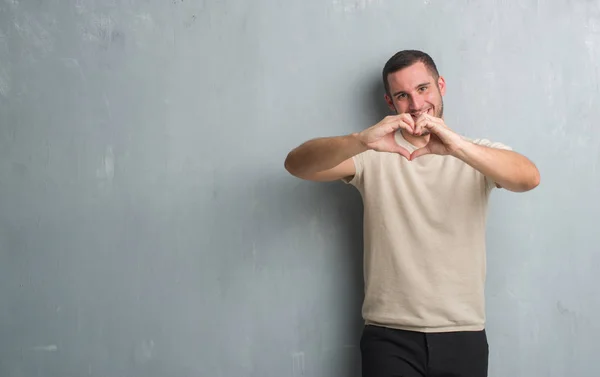 Young Caucasian Man Grey Grunge Wall Smiling Love Showing Heart — Stock Photo, Image