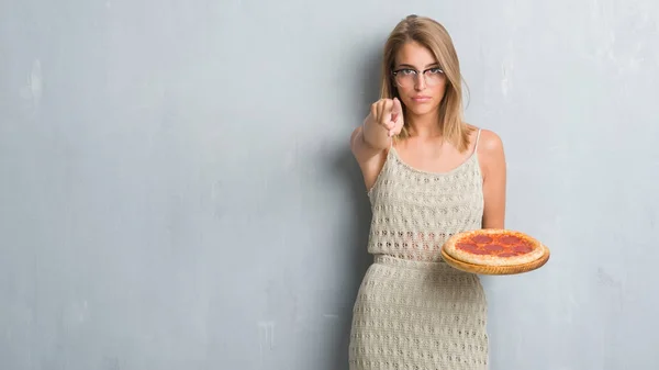 カメラと指で指してペパロニのピザを食べてグランジ灰色の壁に美しい若い女性 手に署名 正面からポジティブで自信のジェスチャー — ストック写真