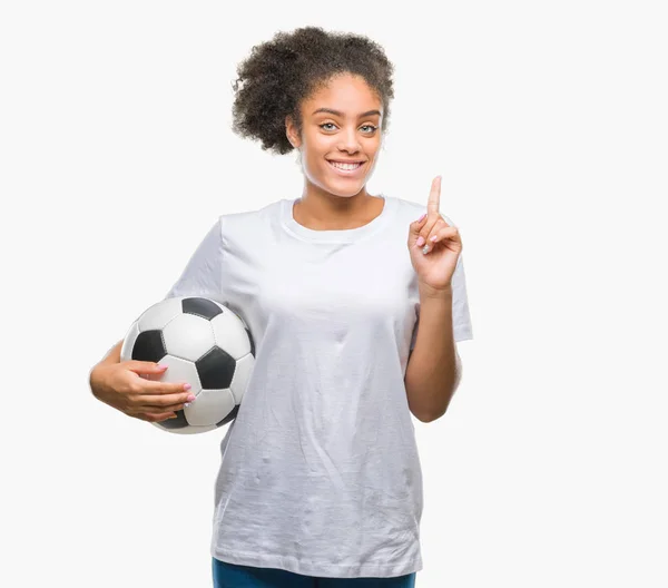 年轻美丽的美国黑人在孤立的背景下举行足球足球球惊讶于一个想法或问题指着一个快乐的脸 — 图库照片