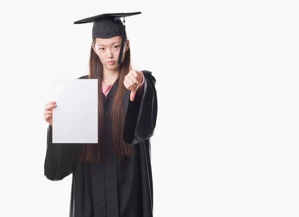 怒った顔 ダウン親指で嫌悪感を示すマイナス記号 拒絶反応の概念との紙程度を保持している大学院の制服を着て若い中国の女性 — ストック写真