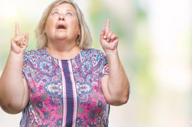 Kıdemli artı izole arka plan üzerinde beyaz kadın hayrete ve yukarıya bakıp parmakları ile işaret şaşırttı ve silah kaldırdı boyutu.