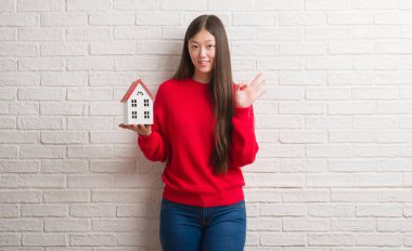 Genç Çinli gerçek durum Aracısı kadın parmakları, mükemmel sembolü olan ok işareti yapıyor tuğla duvar holding ev