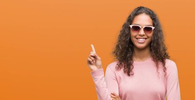 Kameraya bakarak yan el ve parmak ile işaret, yüzünde kocaman bir gülümseme ile güneş gözlüğü takıyor güzel genç İspanyol kadın.