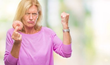 Orta yaş sarışın kadın pembe çörek üzerinde izole yeme arka plan ile öfke, çılgın ve yükseltilmiş eliyle diye bağıran rahatsız ve hayal kırıklığına uğramış öfke kavramı bağırarak