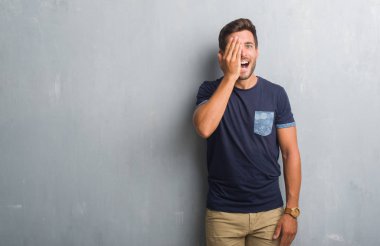 El yüz ve sürpriz duygu kendinden emin gülümseme ile tek gözü kaplayan gri grunge duvarın üzerinden yakışıklı genç.