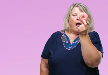 Kıdemli artı boyutu şok bir sürpriz ile kafkas kadın izole arka plan üzerinde şeker donut yemek korkmuş yüz, korkuyor ve heyecanlı korku ifadesi ile