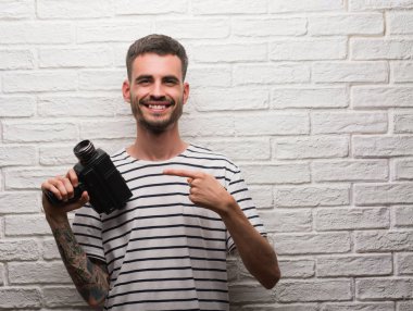 Genç adam tutarak kamerayı beyaz tuğla duvar el ve parmak ile işaret çok mutlu üzerinde duran filme