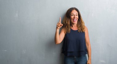 Orta yaş İspanyol kadın başarılı fikir gri grunge duvar işaret parmağı üzerinde ayakta. Çıktıktan ve mutlu. Bir numara.