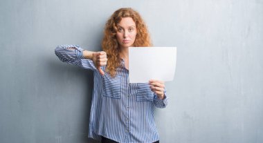 Gri grunge genç Kızıl saçlı kadın duvar kızgın yüzü, eksi işareti aşağı antipati başparmak ile gösterilen, ret kavramı ile boş kağıt levha holding