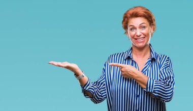 Atrractive üst düzey beyaz Kızıl saçlı kadın hayrete ve el ile sunulması ve parmak ile işaret ederken kameraya gülümseyen izole arka plan.