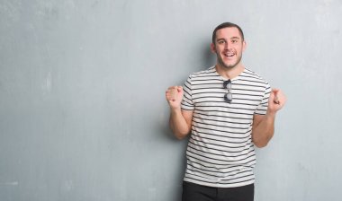 Gri grunge duvar kutluyor üzerinde beyaz delikanlı şaşırttı ve başarı için kaldırdı kollarını açarak hayret ve gözleri açık. Kazanan kavramı.