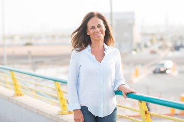 Street yüzünde gülümseme ile duran güzel orta yaş İspanyol kadın. Şehir gezinti güvenli ve neşeli güneşli bir günde gülümseyen denizin kenarında yürüyüş.