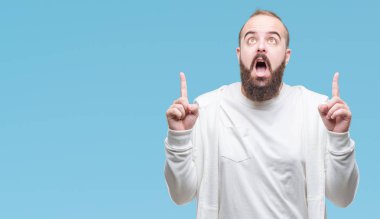 Spor kıyafetlerle izole arka plan üzerinde genç beyaz hipster adam hayret ve yukarıya bakıp parmakları ile işaret şaşırttı ve silah kaldırdı.