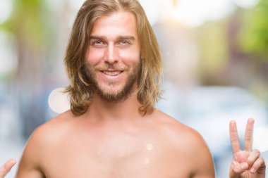 Genç yakışıklı gömleksiz adam uzun saçlı seksi vücut gösterilen ve parmakları ile işaret izole arka plan üzerinde gösterilen kendinden emin ve mutlu gülümseyerek süre yedi numara.