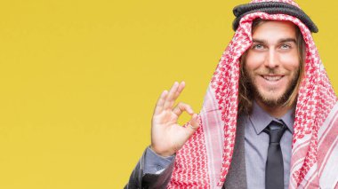 Genç yakışıklı Arap adam uzun saçlı keffiyeh izole arka plan el ve parmaklar ok işaretiyle yapıyor olumlu gülümseyen üzerinde giyiyor. Başarılı ifade.