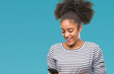 İzole arka plan üzerinde duran ve diş gösterilen kendine güvenen bir gülümsemeyle gülümseyerek mutlu bir yüz ile Smartphone kullanarak genç afro Amerikalı kadın manifatura