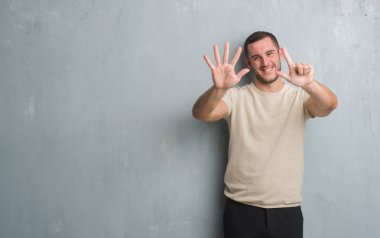 Gösterilen ve parmakları ile işaret gri grunge duvarın üzerinden Genç beyaz adam kendinden emin ve mutlu gülümseyerek süre yedi numara.