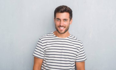 Uzak tarafına yüzünde, doğal ifade gülümseme ile seyir lacivert t-shirt giyen gri grunge duvarın üzerinden yakışıklı genç adam. Kendine güvenen gülüyor.