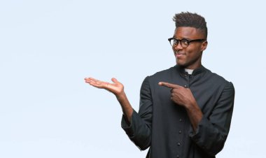 Genç Afro-Amerikan rahip adam üzerinden hayran ve el ile sunulması ve parmak ile işaret ederken kameraya gülümseyen izole arka plan.