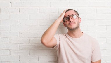 Genç beyaz adam baş, el ile vurguladı gözlüklü beyaz tuğla duvarın üzerinden ayakta şok utanç ve sürpriz suratla, öfkeli ve sinirli. Korku ve hata için üzgün.