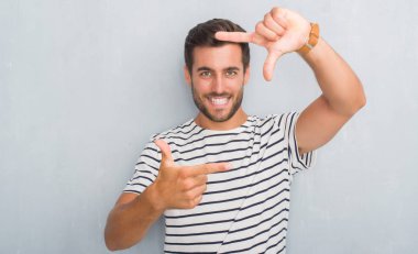 Elle yapma çerçeve ve parmakları ile mutlu yüz gülümseyen lacivert t-shirt giyen gri grunge duvarın üzerinden yakışıklı genç adam. Yaratıcılık ve Fotoğrafçılık kavramı.