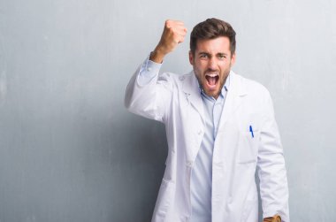 Yakışıklı genç profesyonel adam kızgın ve hayal kırıklığı ve öfke ile bağırarak süre öfkeli yumruk yükselterek deli beyaz önlük giyen gri grunge duvarın üzerinden. Öfke ve agresif kavramı.