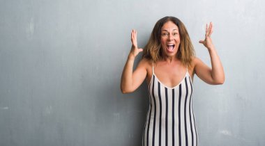 Kocaman bir gülümseme ile çığlık zaferini kutluyor gri grunge duvar çok mutlu ve heyecanlı, kazanan ifade üzerinde duran ve ellerini kaldırdı orta yaş İspanyol kadın