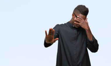 Genç Afrikalı-Amerikalı rahip adam elleriyle gözlerini kapsayan izole arka plan üzerinde ve stop jest ile acı ve korku ifadesi. Utandım ve negatif kavramı.