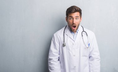Yakışıklı genç doktor adam gri grunge duvarın korkuyor ve şok sürpriz ifade, korku ve heyecan yüz üzerinden.