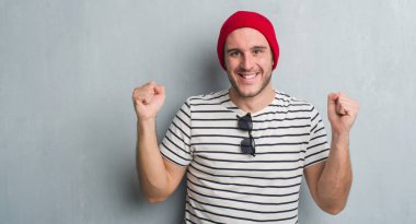 Duygu tezahürat Genç beyaz adam gurur çığlık ve zafer ve başarı çok heyecanlı, kutluyor yün şapkası gri grunge duvarın üzerinden