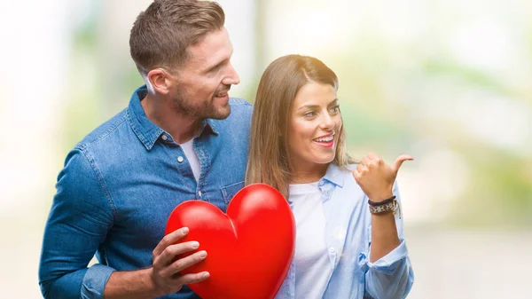 年轻夫妇在爱持有红色心脏在孤立的背景指向和显示与拇指向上的一面微笑的笑脸 — 图库照片