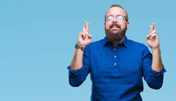 Young caucasian hipster man wearing glasses over isolated background smiling crossing fingers with hope and eyes closed. Luck and superstitious concept.