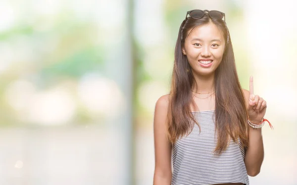 年轻的亚洲妇女戴着太阳镜在孤立的背景显示 并指出手指第一 而微笑着自信和快乐 — 图库照片