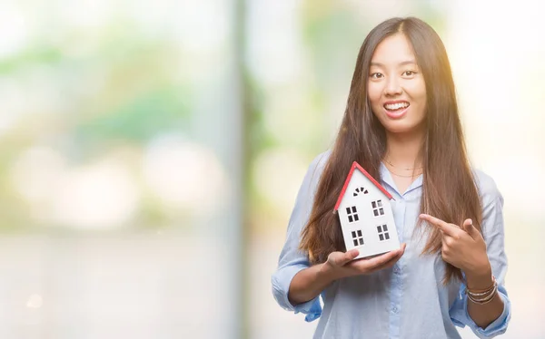 Young asian woman real state agent holding house isolated background very happy pointing with hand and finger